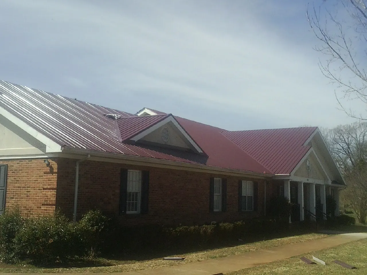 Red metal roof with gabled entries on a long brick building, from a Hail Damage Roof Repair job in Newtonville