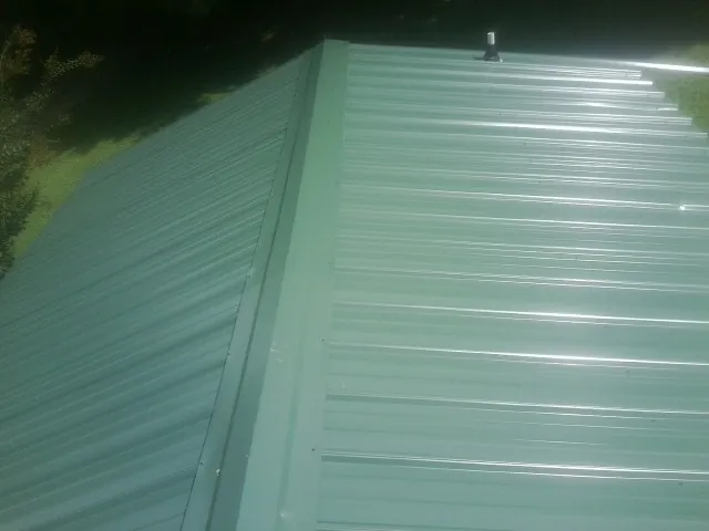 New green metal panels meeting at the ridge of a roof — Flat Roof Repair work by our crew in Newtonville