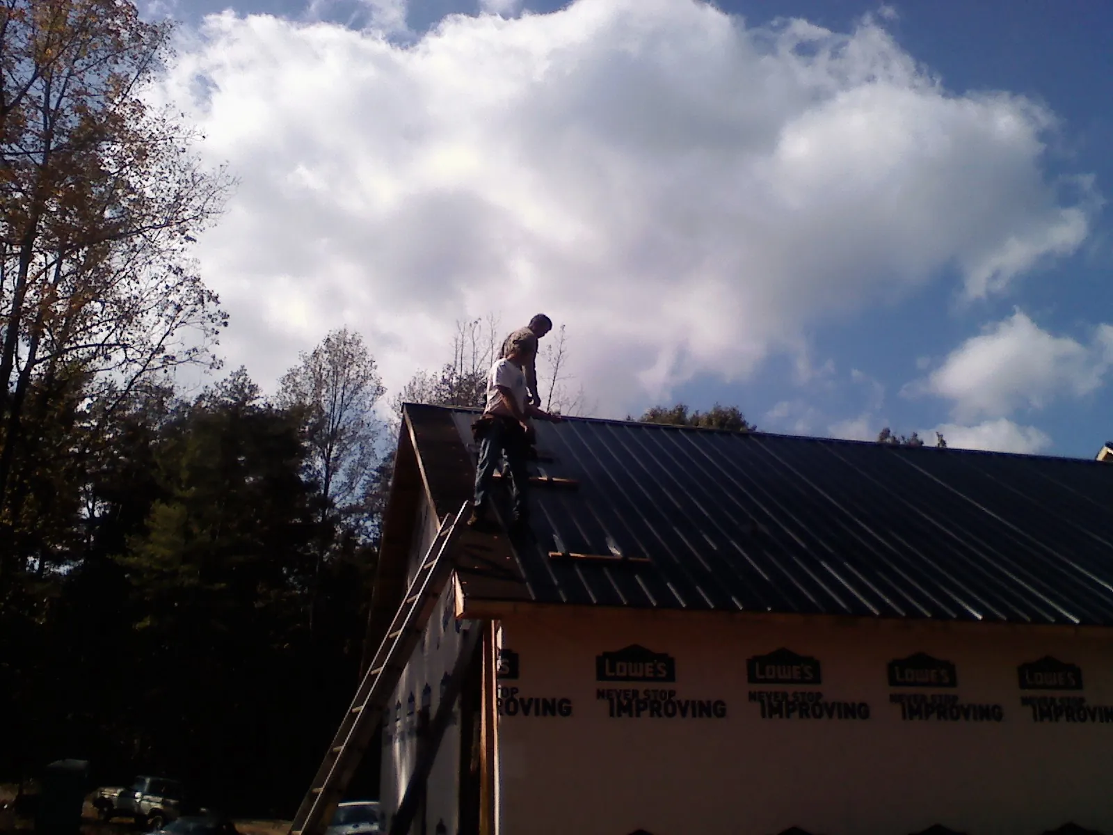 Roofer fastening dark metal panels high against a cloudy sky in Newtonville
