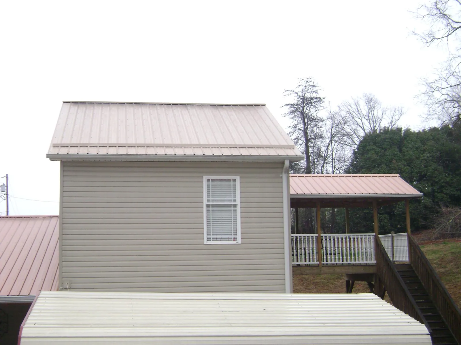 Tan metal roofs on a two story addition and attached porch, from a Roof Replacement job in Newtonville